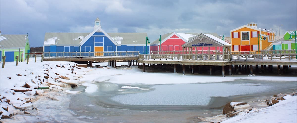A pier with colorful buildings, a snowy landscape, and a frozen body of water.