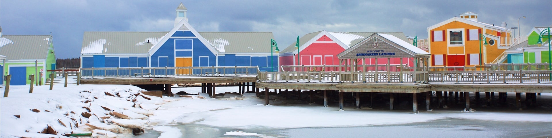 A pier with colorful buildings, a snowy landscape, and a frozen body of water.