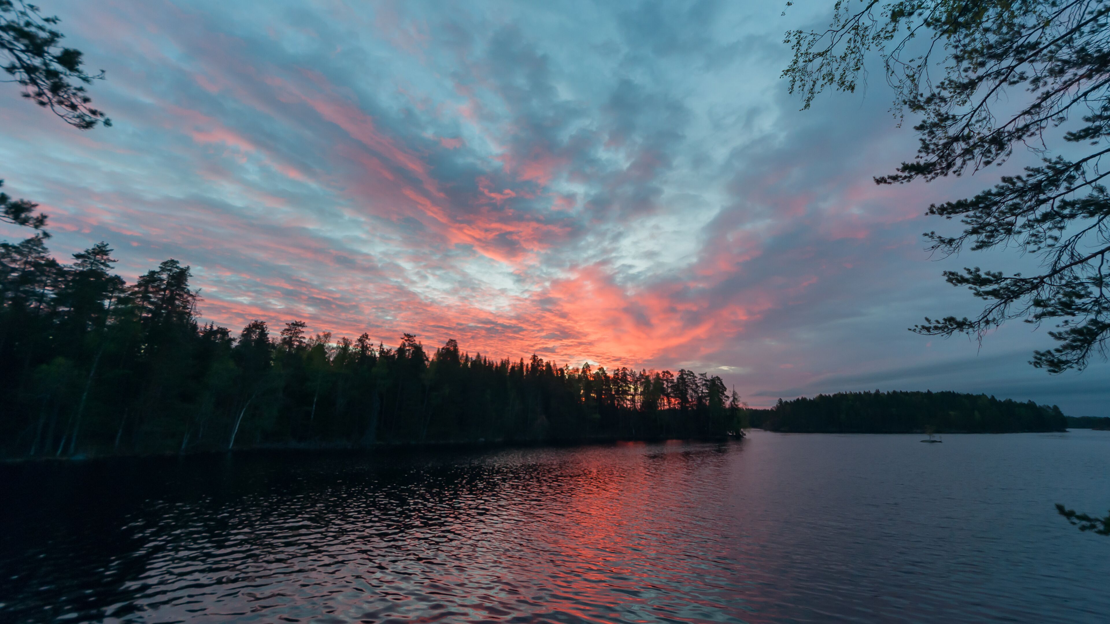 A sunset over a calm lake with a forested shoreline.
