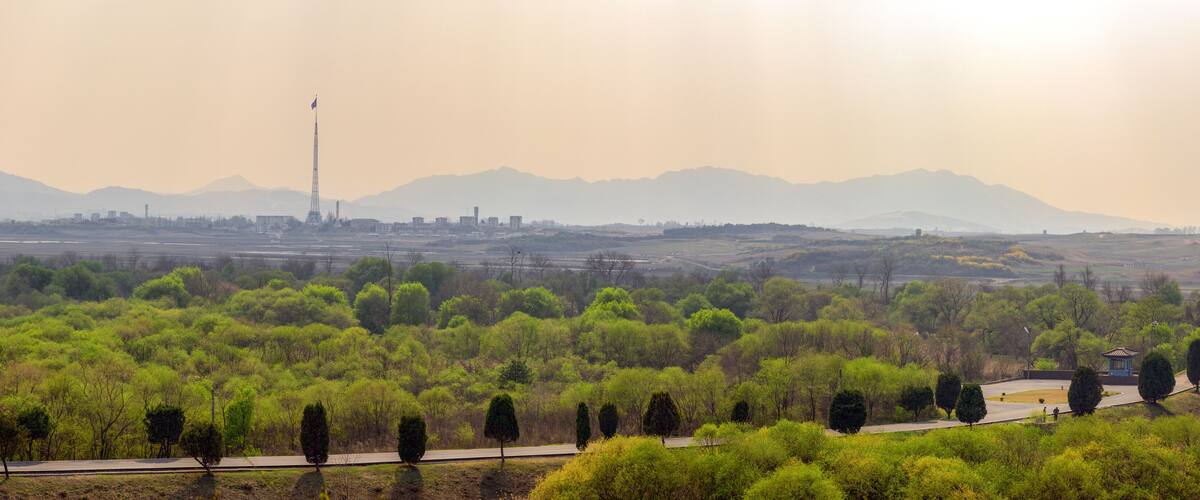 A landscape with a tower, trees, and distant mountains.