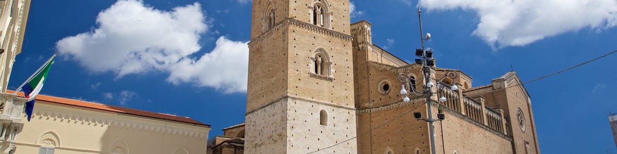 A historic tower with a clock, set against a clear blue sky with scattered clouds.