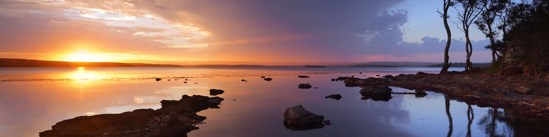 A sunset over a calm lake with rocks and trees.