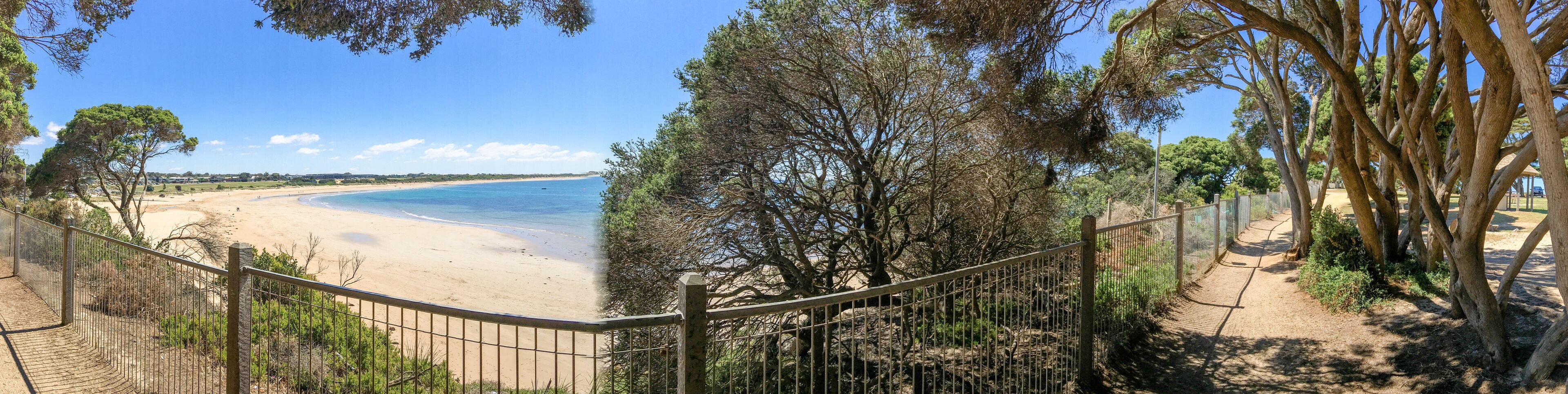A beach with a fence and trees in the foreground.