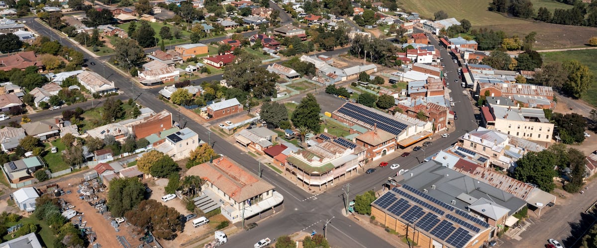 An aerial view of a town with a central street, surrounding buildings, and open fields.
