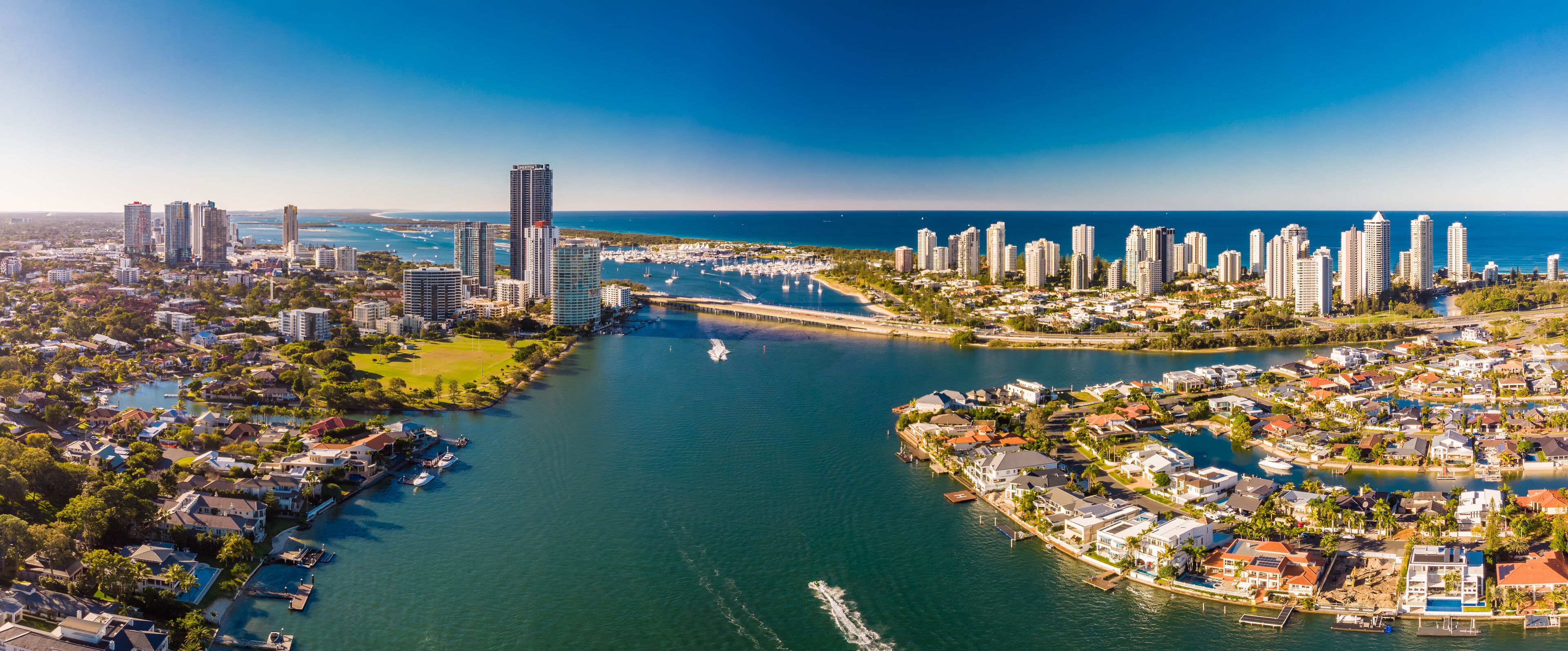 A coastal cityscape with high-rise buildings, a marina, and a river.