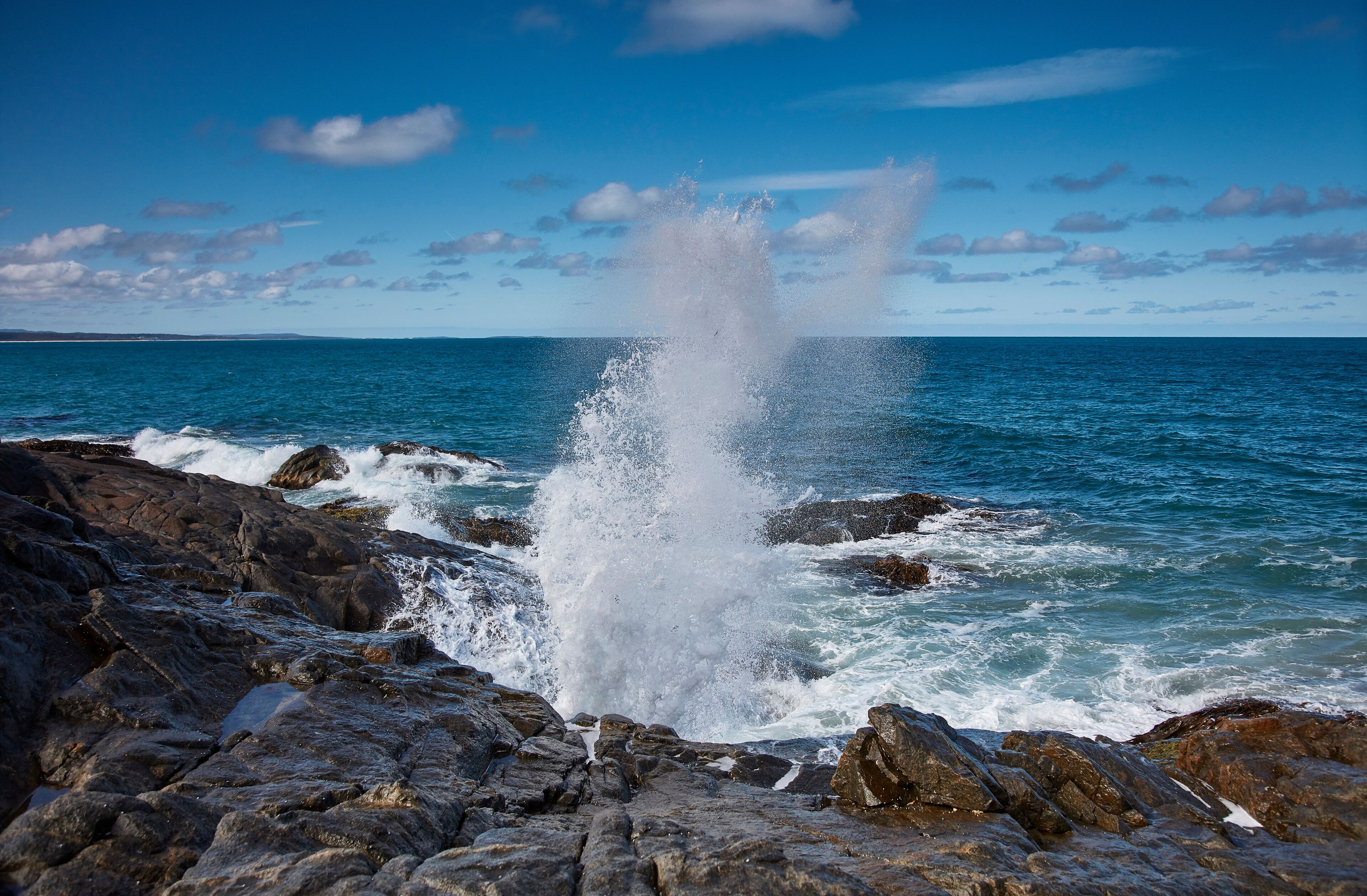 A rocky coastline with waves crashing against the rocks and a clear blue sky.