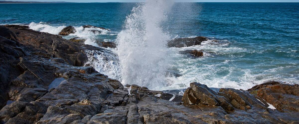 A rocky coastline with waves crashing against the rocks and a clear blue sky.