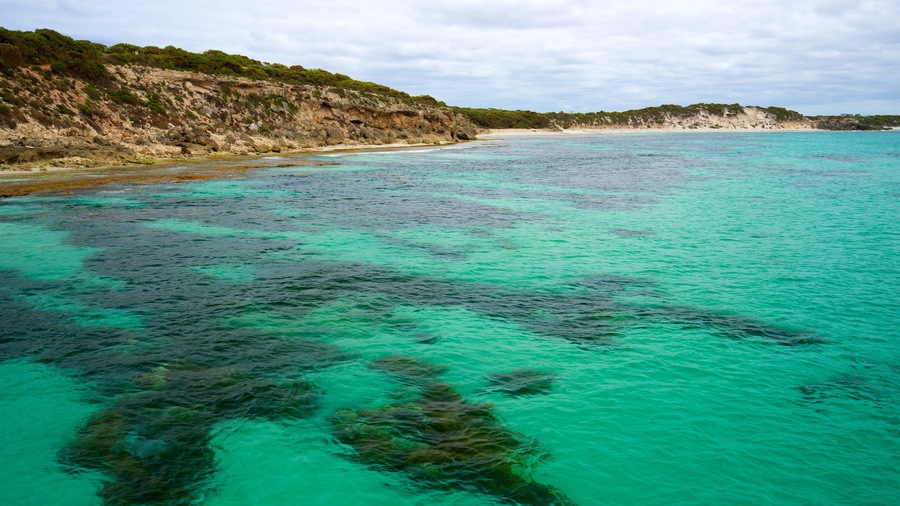 A coastal landscape with clear turquoise waters, rocky cliffs, and a sandy beach.