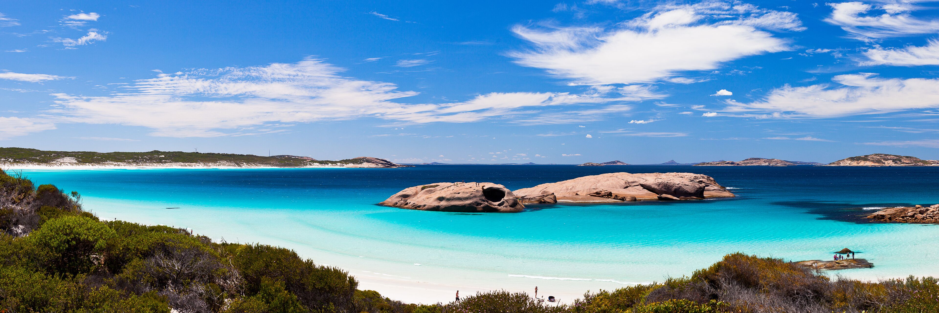 A coastal landscape with clear turquoise waters, rocky formations, and a sandy beach.