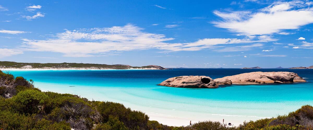 A coastal landscape with clear turquoise waters, rocky formations, and a sandy beach.