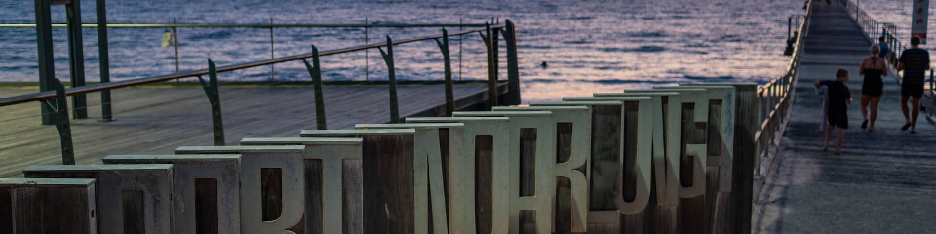 A pier with the words "PORT HARIGON" on the side, overlooking the sea at sunset.