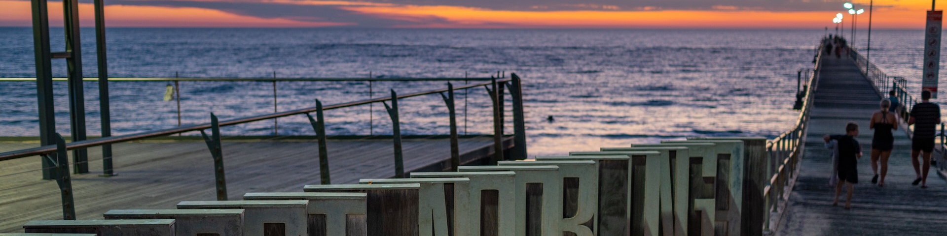 Un muelle con la inscripción "PORT HARIGON" a un lado, con vista al mar al atardecer.