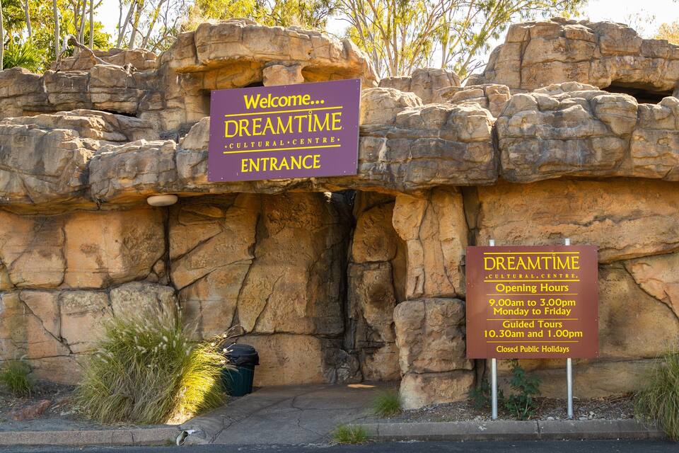 Entrada rocosa al Dreamtime Cultural Centre, con señalización que indica horarios de apertura y horarios de visitas guiadas.