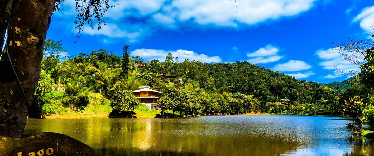 A serene lake with a wooden sign reading "Lago Betão," surrounded by lush greenery and a clear blue sky.