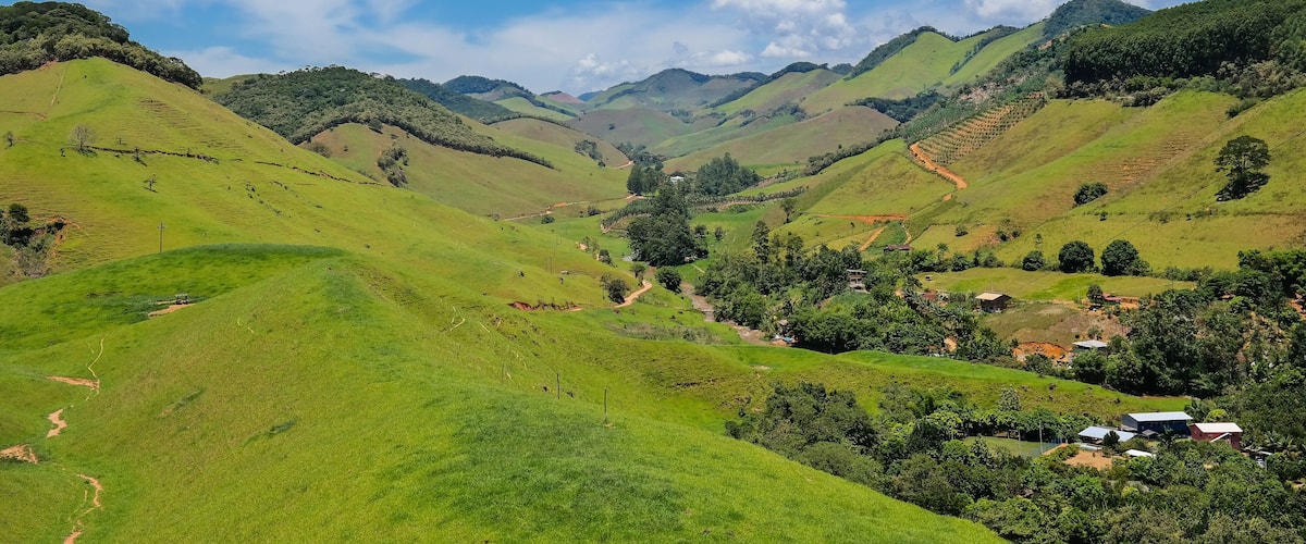 Rolling green hills, a small village, and distant mountains under a clear blue sky.
