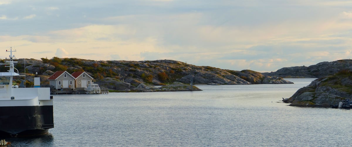 A calm harbor with a large boat docked, surrounded by rocky hills and small houses.