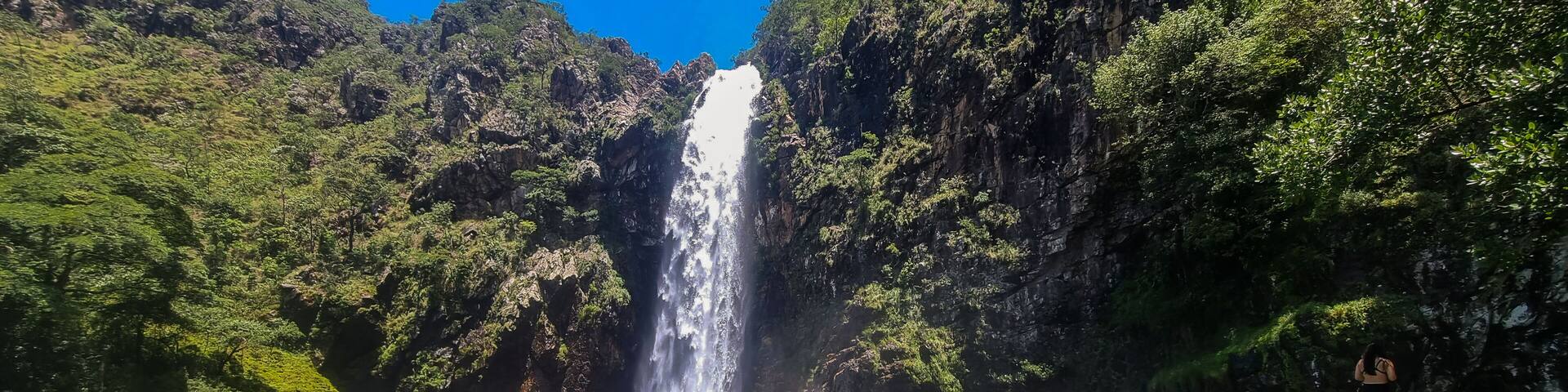 A waterfall cascading into a clear river surrounded by lush greenery and rocky cliffs.
