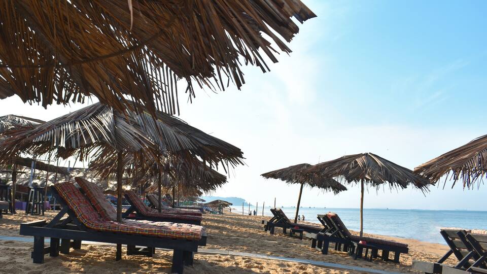 A beach with lounge chairs and thatched umbrellas.