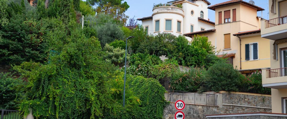 A residential area with Mediterranean architecture, lush greenery, and a stone wall with a speed limit sign.