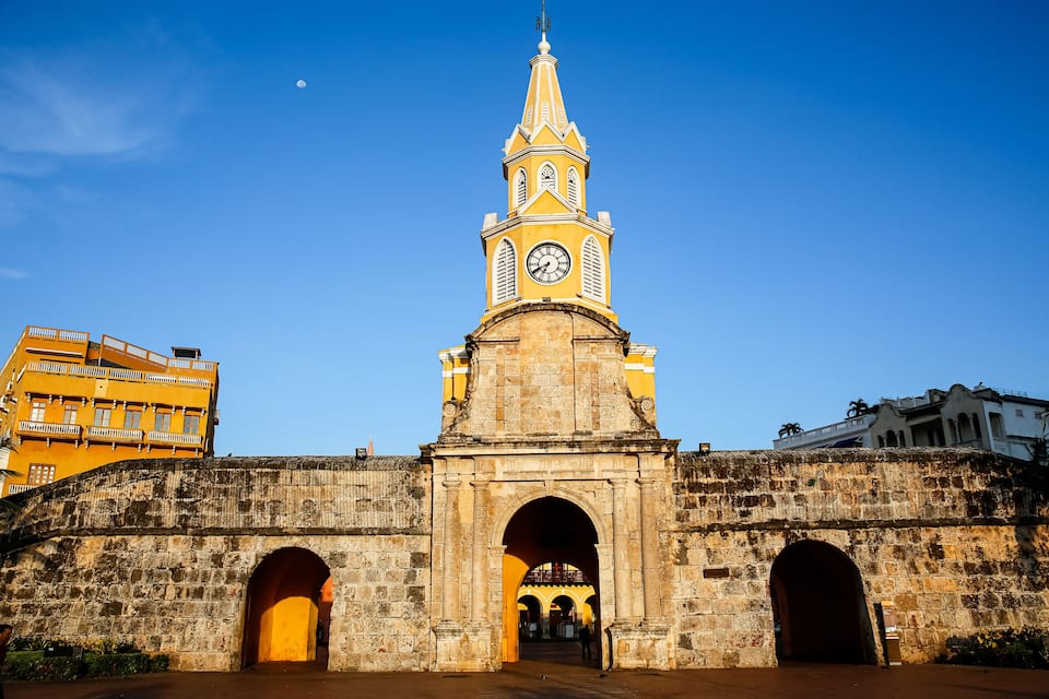 A historic stone bridge with arches, a clock tower, and a clear blue sky.