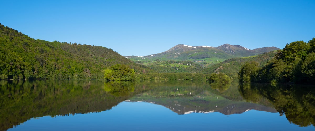 A calm lake reflecting a mountainous landscape with dense forests on either side.