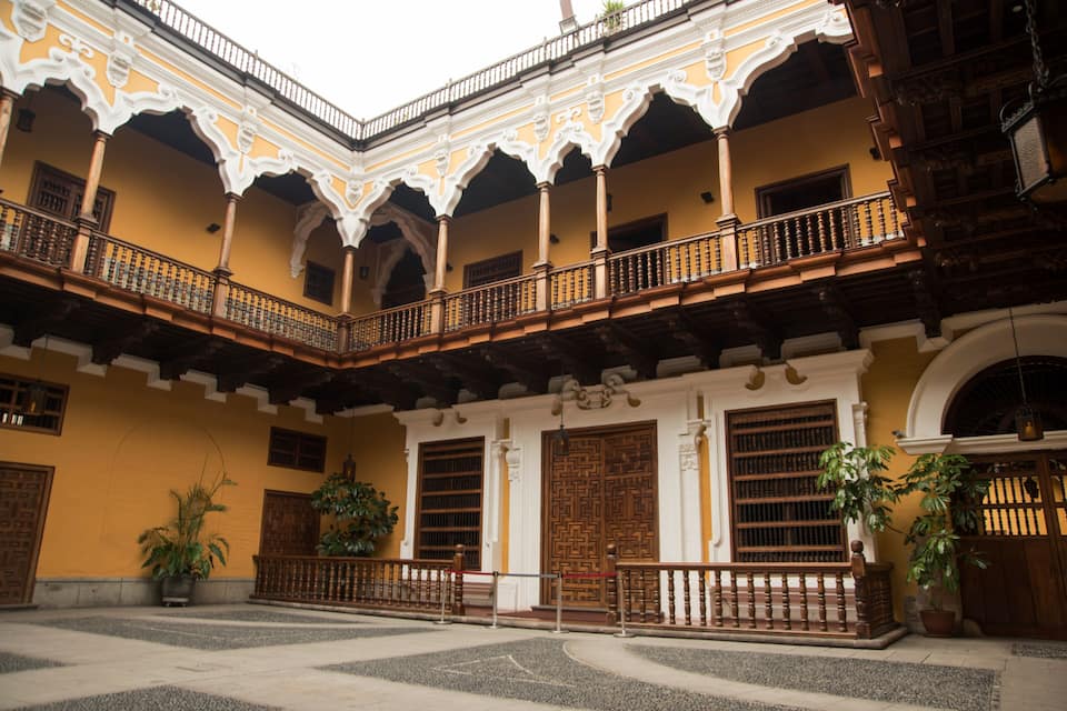 Un cortile con balconi decorati, porte in legno e piante in vaso.