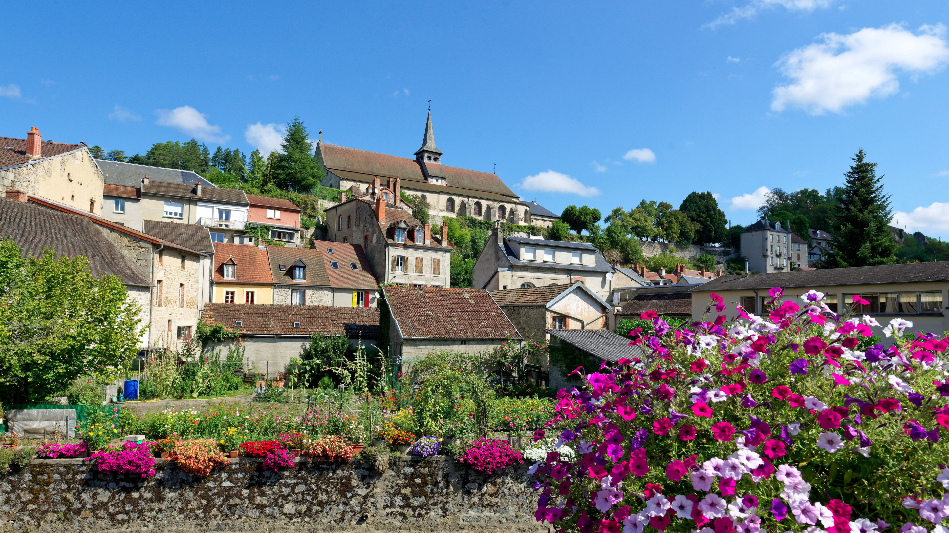 A hillside town with historic buildings, a church, and vibrant gardens.