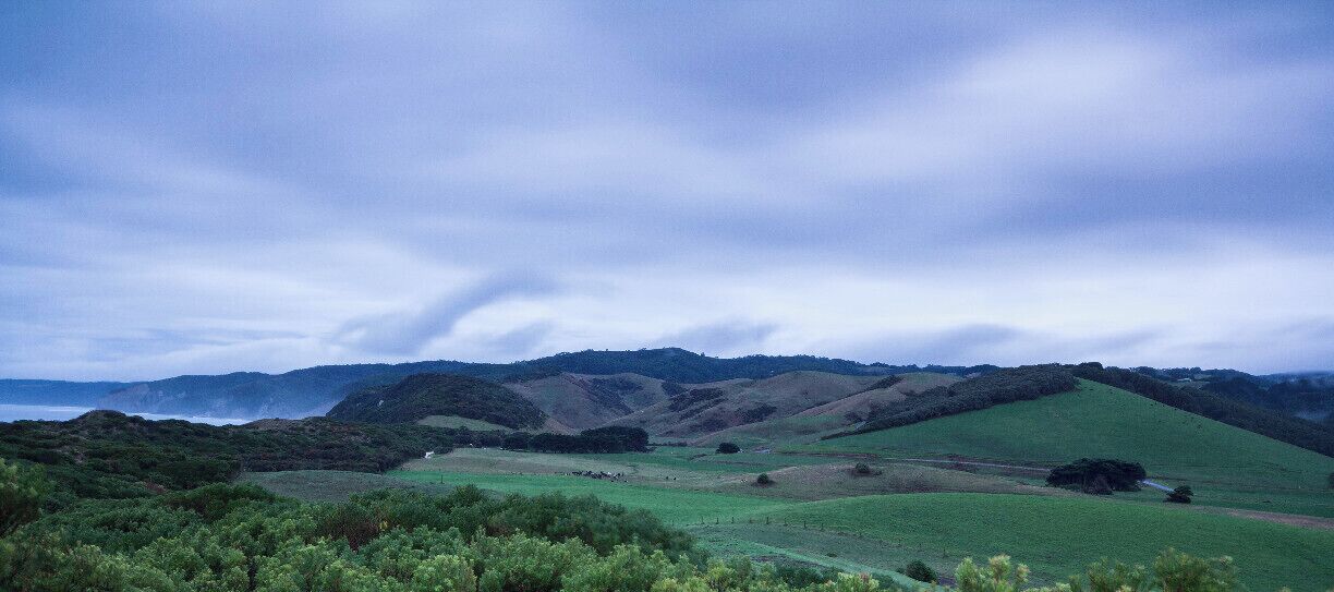 Rolling hills, a distant body of water, and a cloudy sky.