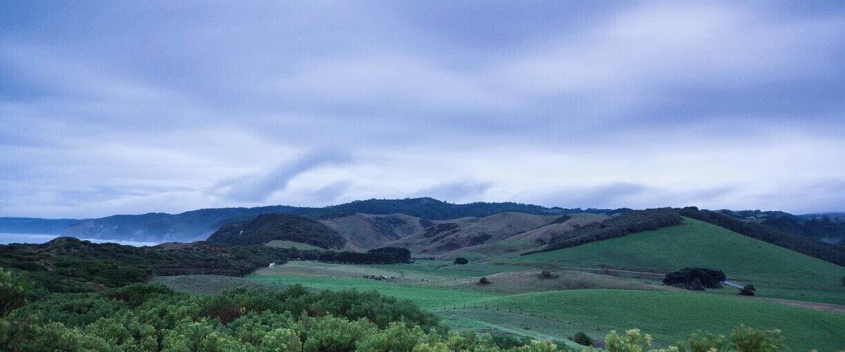 Rolling hills, a distant body of water, and a cloudy sky.