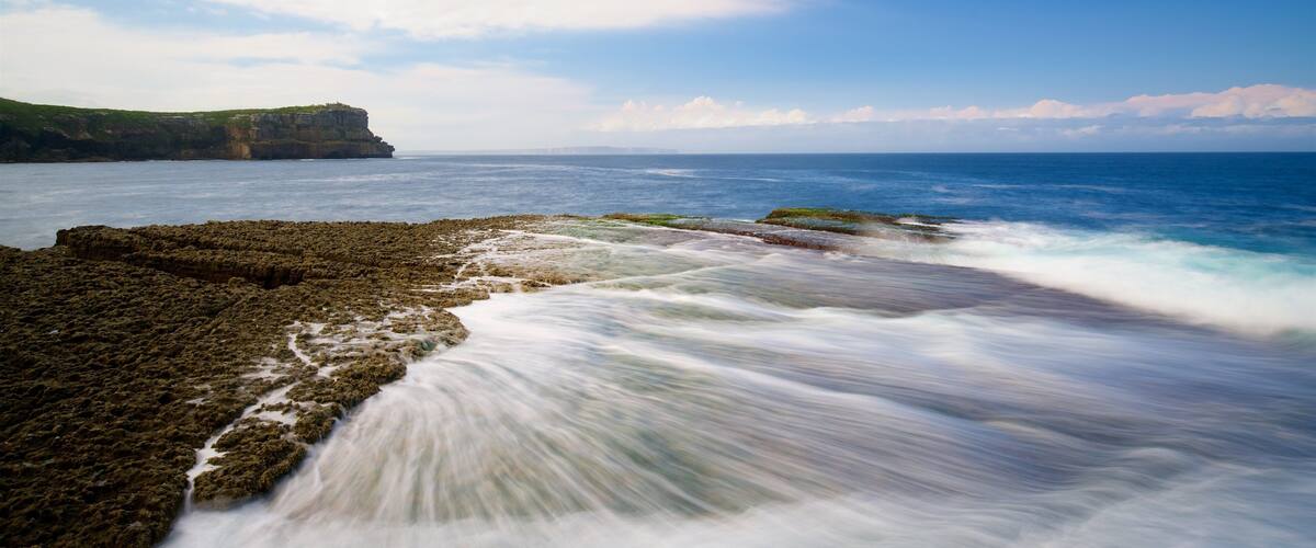 A rocky coastline with waves crashing onto the shore under a clear sky.