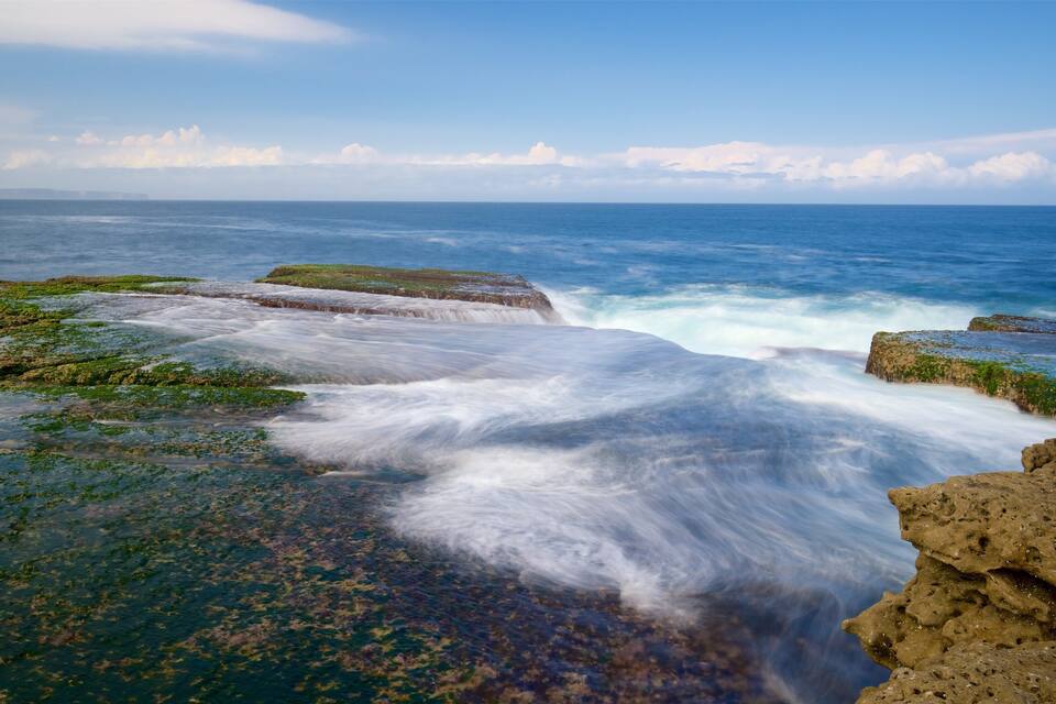 A coastal landscape with rocky formations and waves crashing against them.
