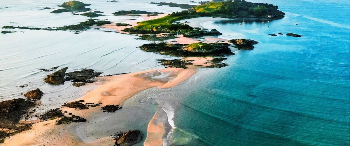 A coastal landscape with a sandy beach, rocky outcrops, and a small island with vegetation.