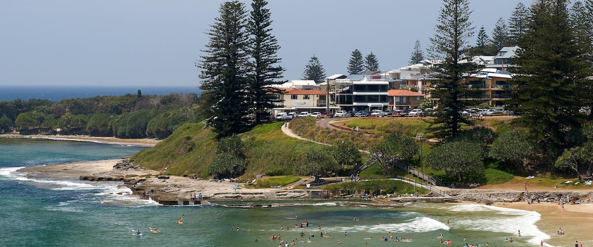 A coastal town with a beach, ocean, and buildings on a hillside.