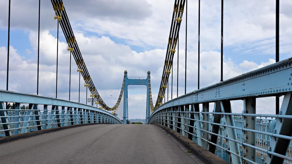 A blue suspension bridge with a clear sky and clouds in the background.