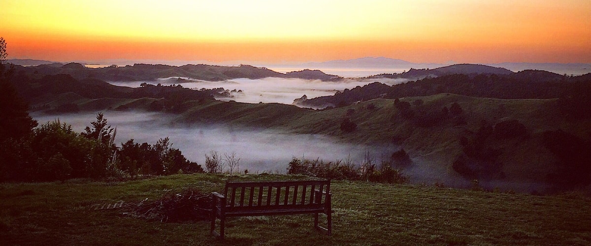 A bench overlooking a valley with mist-covered hills and a sunset in the background.