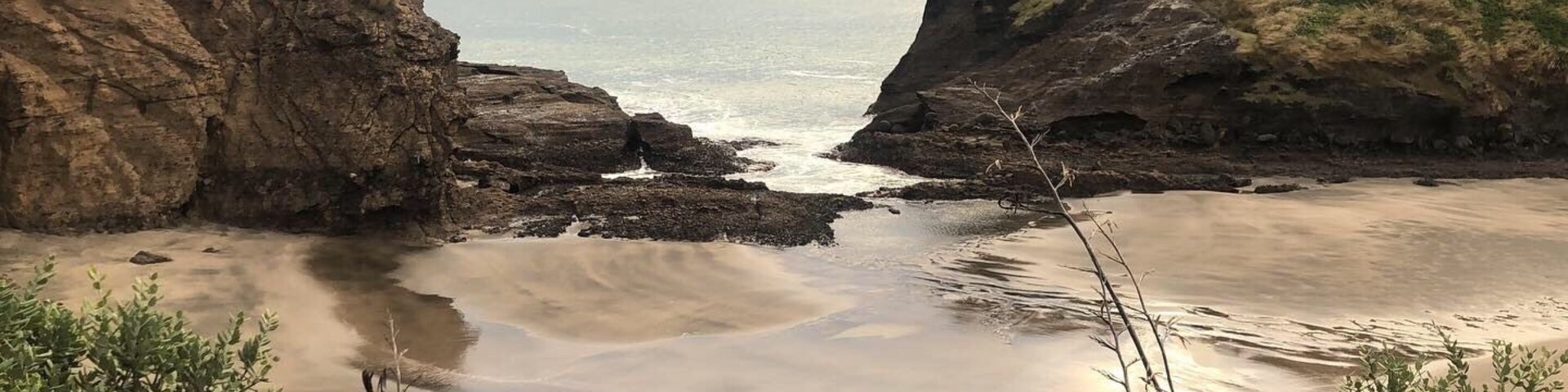 Paisagem costeira com falésias rochosas, uma praia arenosa e mar calmo.