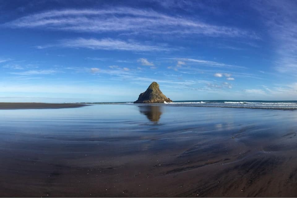 Ein Strand mit einer großen Felsformation im Wasser.