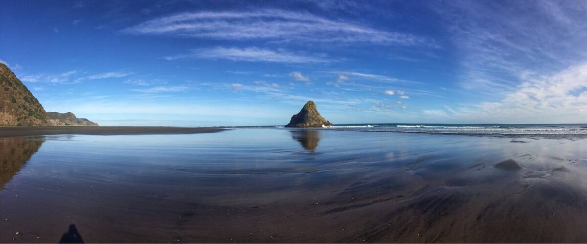 A beach with a large rock formation in the middle of the water.