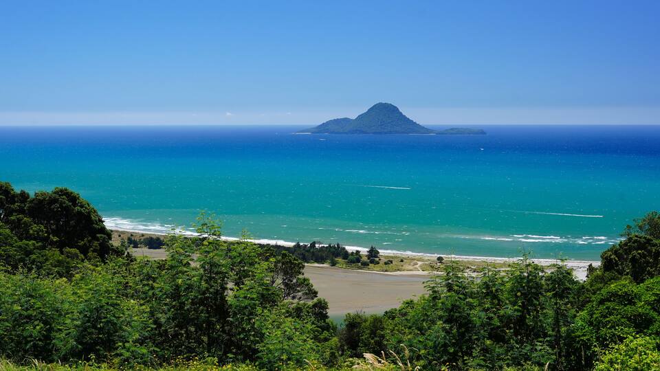 A coastal landscape with a prominent hill, a beach, and the ocean.