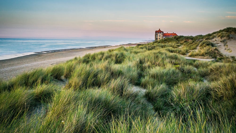 Un paysage côtier avec des dunes, une plage et un bâtiment situé sur une colline.