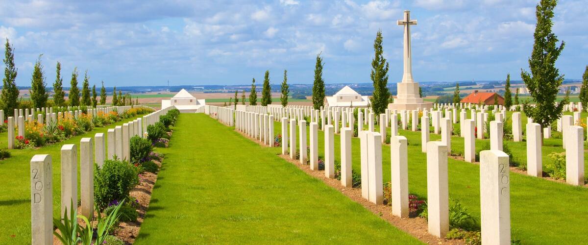 A cemetery with rows of white headstones and a central cross monument.
