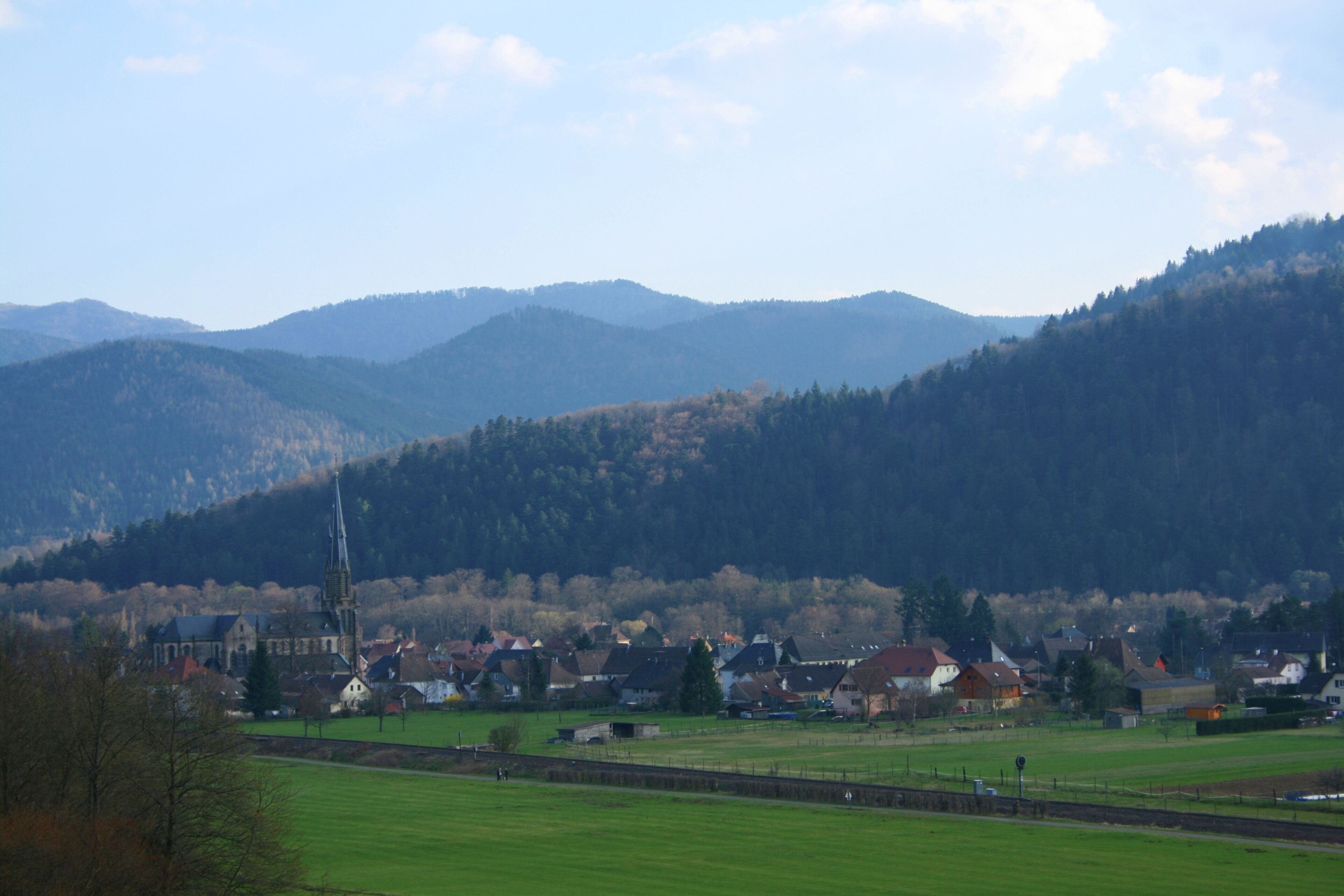 A rural landscape with a church, houses, and rolling hills.