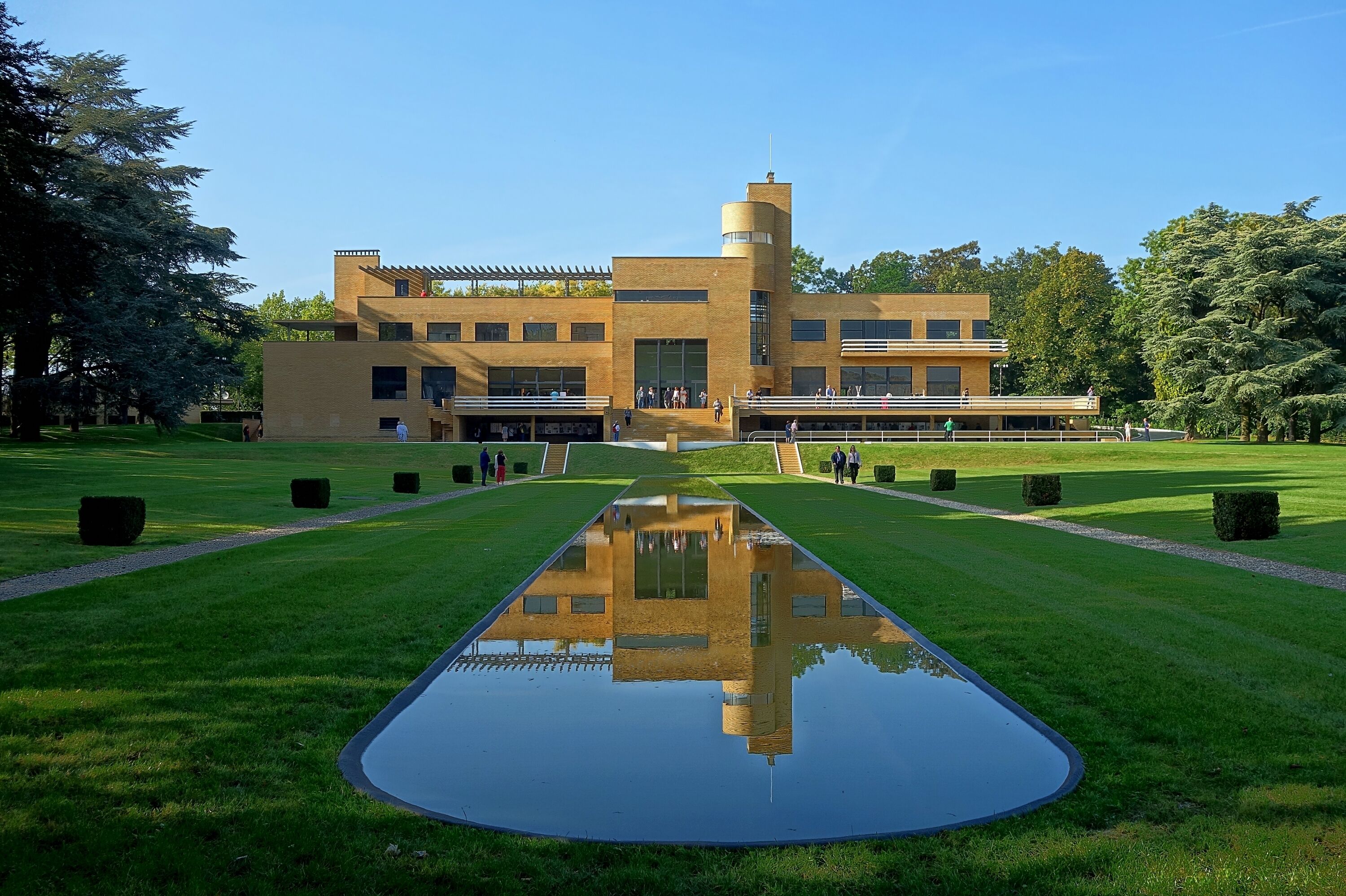 A modern building with a central tower, surrounded by a well-manicured lawn and a reflective water feature.