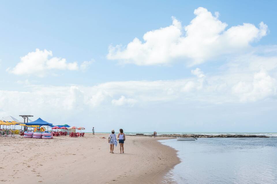 Una playa arenosa con sombrillas, una torre de salvavidas y un mar tranquilo.