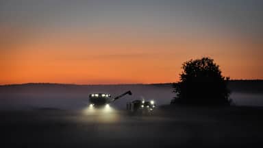 Combine harvester and tractor harvesting grains late at night in mist covered fields in the farmland of meteor impact crater Söderfjärden in Korsholm or Vaasa, in the region of Ostrobothnia, Finland.