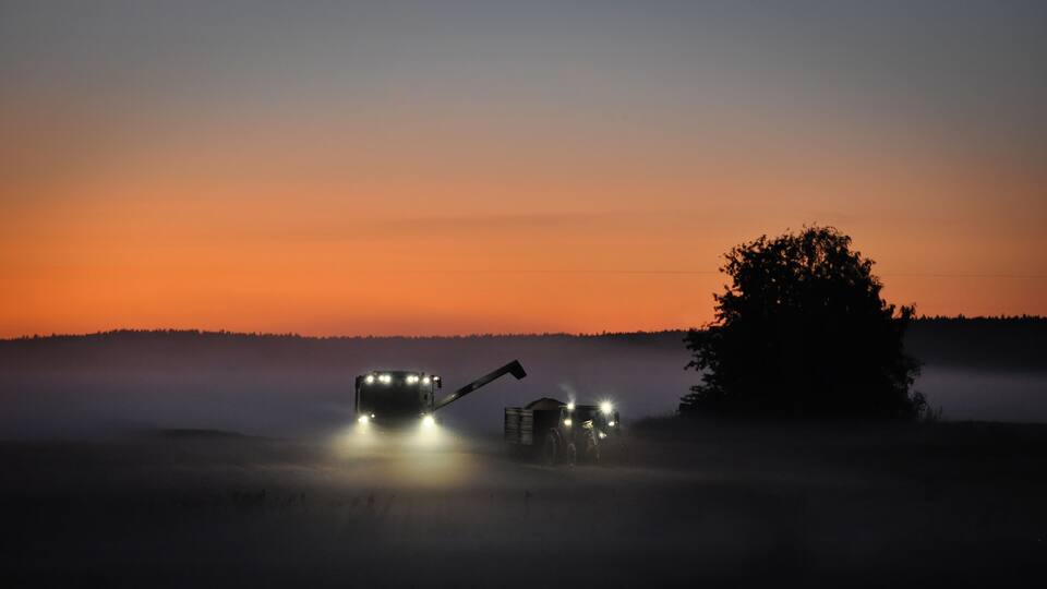 A combine harvester in a foggy field at dusk.