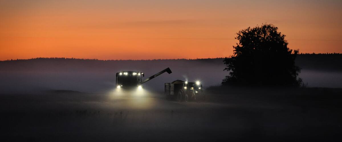 A combine harvester in a foggy field at dusk.