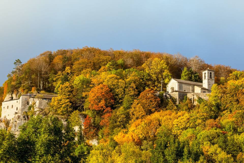 A historic stone church on a hill surrounded by autumn-colored trees.