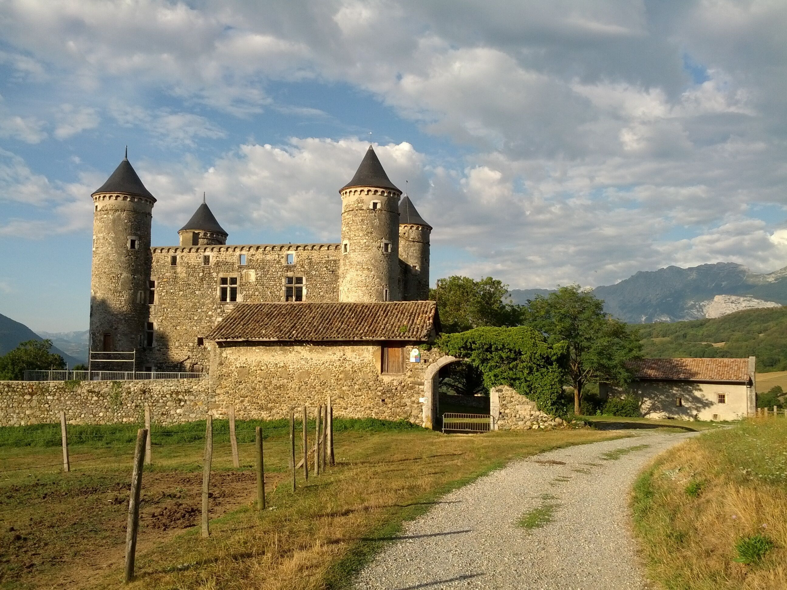 A medieval castle with two towers, surrounded by a stone wall and a gravel path.