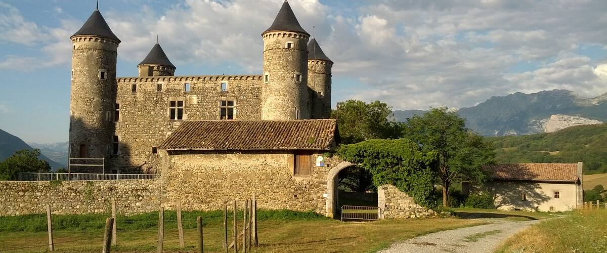 A medieval castle with two towers, surrounded by a stone wall and a gravel path.